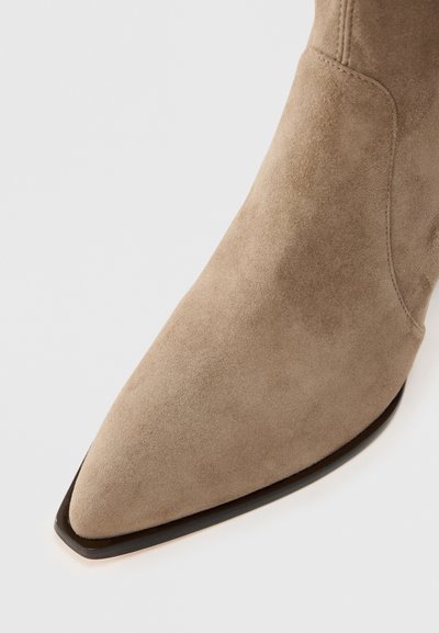 Beige suede ankle boot with a pointed toe and a black textured sole. The upper features a smooth finish and subtle stitching details.