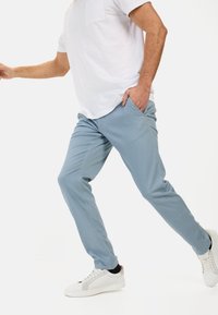 Lichtblauwe casual broek gemaakt van stof met een gladde textuur. Draagt een wit t-shirt en witte sneakers. Eenvoudig ontwerp, geen patronen.