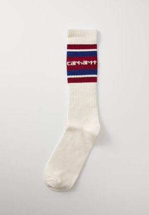Knee-high socks in cream, featuring a ribbed design with red, blue, and white stripes. "Carhartt" logo displayed on the band.