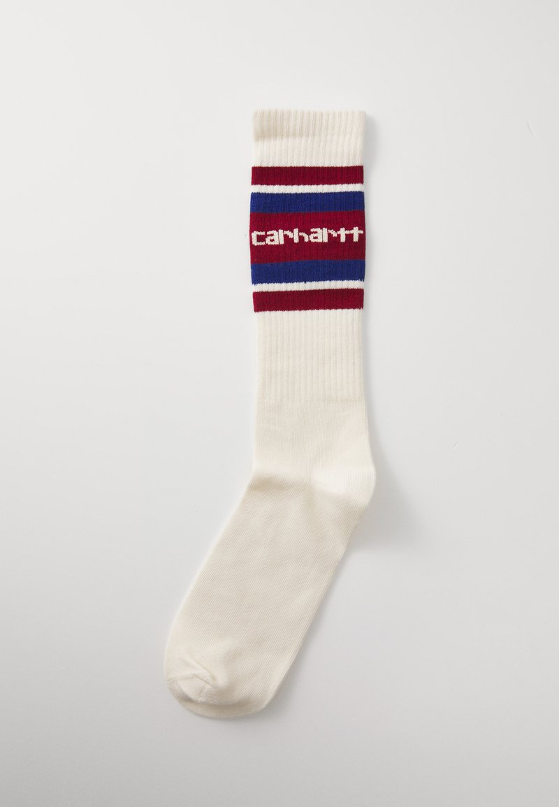 Knee-high socks in cream, featuring a ribbed design with red, blue, and white stripes. "Carhartt" logo displayed on the band.