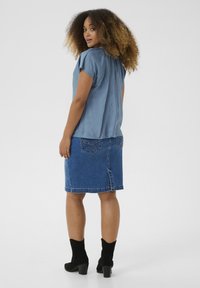 Haut bleu clair à manches courtes associé à une jupe en jean. La jupe comporte une fente à l'arrière et deux poches arrière. Des bottines noires à la cheville complètent le look.