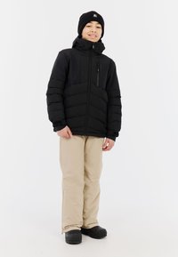 Schwarze, gepolsterte Jacke mit hohem Kragen, Reißverschlusstaschen und elastischen Bündchen, kombiniert mit beigen Hosen und schwarzen Stiefeln. Einfaches Design.