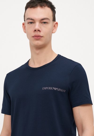 Tamsiai mėlynas medvilninis marškinėliai su apvaliu iškirpimu ir trumpomis rankovėmis. Krūtinėje yra mažas, šviesios spalvos "Emporio Armani" logotipas.