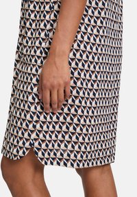 Šaty s krátkým rukávem s geometrickým vzorem v námořnické modři, krémové a hnědé, s křivkovým lemem a bočními kapsami. Bavlněný materiál.