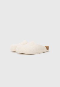 Zuecos de fieltro blancos con punta redondeada, textura lisa y suela de corcho. El diseño presenta un silueta fácil de poner sin correas tradicionales.