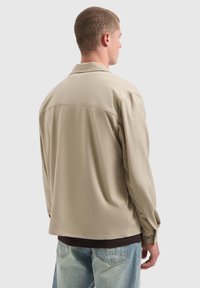 Beige langpoloshirt met een relaxte pasvorm, platte kraag en met knopen sluitende manchetten. Glad textuur met details van een naad op de rug.