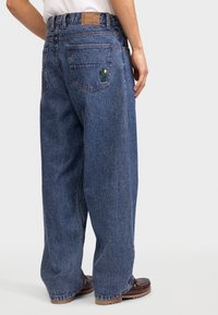 Blauwe denim jeans met een ontspannen pasvorm, voorzien van een cactusborduursel op de achterzak en een bruine leren taillebandlabel.