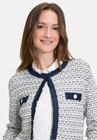 Weiße und marineblaue Tweed-Cardigan mit rundem Kragen, strukturiertem Muster, fransigen Kanten und zwei aufgesetzten Taschen mit Knöpfen.