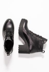 Black leather ankle boots with a chunky, scalloped heel. Features include a lace-up front, textured finish, and a pull tab at the back.