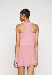 Pink sports dress with a fitted bodice and flared skirt. Features a racerback design and a hemline with perforated detailing. Smooth texture.