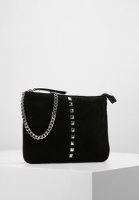 Czarna zamszowa kopertówka z srebrnym łańcuszkowym paskiem, zdobiona linią srebrnych ćwieków na przodzie. Zamykanie na suwak u góry.