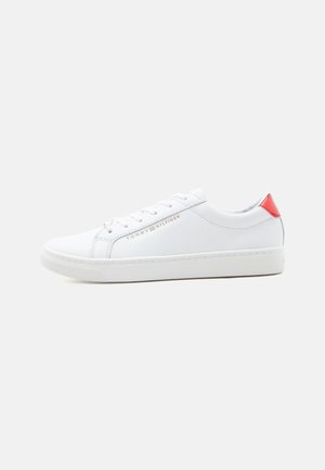Baskets basses blanches avec un design à lacets, logo doré "Tommy Hilfiger" sur le côté et accent rouge sur la languette du talon.