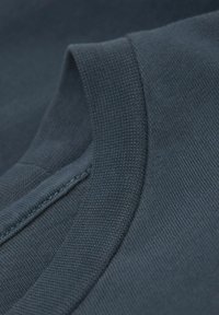 Tmavě modré bavlněné tričko zblízka, s žebrovaným límcem a precizním švem. Měkká textura s hladkým, jednolitým materiálem.