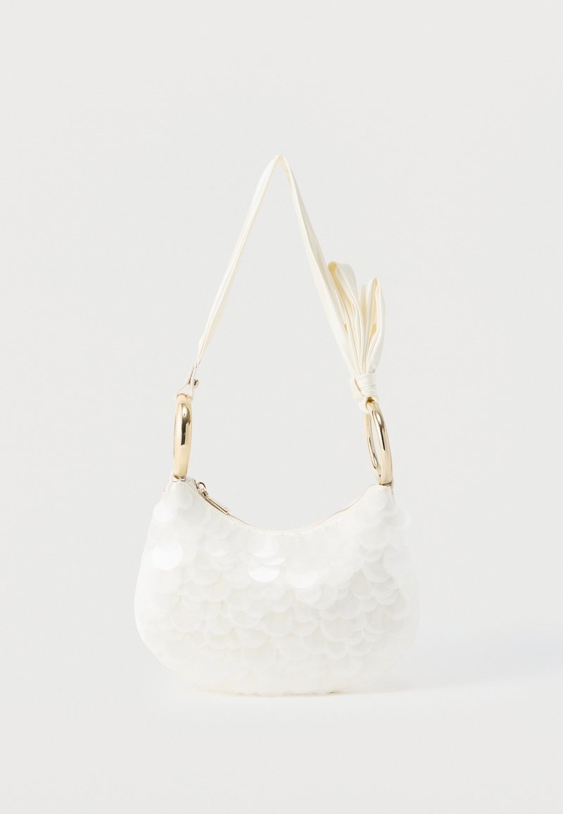 Λευκή τσάντα ώμου με μεγάλα στρογγυλά παγιέτες, χρυσαφένιες μεταλλικές λαβές σε σχήμα δαχτυλιδιού και δεμένη υφασμάτινη λουρίδα σε απλό φόντο.