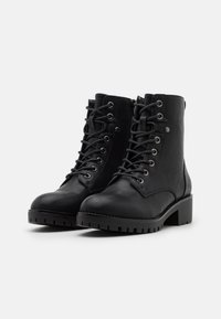 Botas de tobillo de cuero negro con diseño de cordones, ojales metálicos, cuello acolchado y tacón bajo grueso con suela de goma.