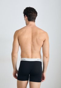 Fekete pamut boxer alsónadrág fehér Calvin Klein logós derékpánttal. A modell hátulról látható, bemutatva a sima textúrát és a testhez simuló fazont.