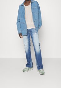 Chaqueta vaquera azul claro con dos bolsillos delanteros, camisa de punto beige, vaqueros azules desgastados y zapatillas verdes con estampado.