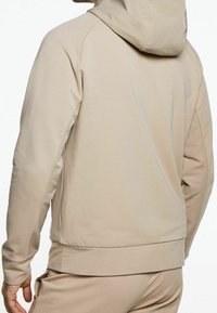 Sudadera con capucha beige hecha de un tejido suave, con un corte relajado y puños de canalé. El diseño tiene una textura simple y suave.