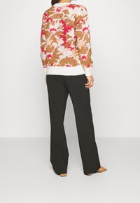 Pull en laine avec un motif floral dans des tones de marron, rose et crème ; poignets côtelés blancs. Assorti avec un pantalon large noir et des sandales ouvertes.