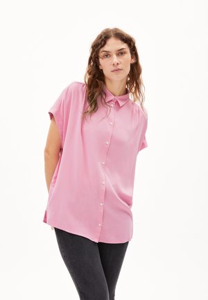 Pink short-sleeve button-up shirt with a collar, featuring a smooth texture and a relaxed fit, worn with dark jeans.