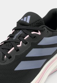 Zwart sportief schoen met een bovenwerk van mesh, lichtroze accenten en drie gestructureerde grijze strepen aan de zijkant. Veters zijn zwart en stevig aangedraaid.