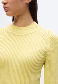 Κίτρινο πλεκτό πουλόβερ με ριγέ υφή, ψηλή λαιμόκοψη και εφαρμοστή γραμμή, με απαλό ύφασμα και διαγώνιες ραφές στα μανίκια.