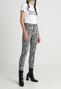 Camiseta blanca con texto negro, combinada con jeans ajustados de estampado de serpiente en blanco y negro y botas altas de charol negras.