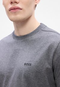 Γκρίζα βαμβακερή μπλούζα με στρογγυλή λαιμόκοψη και ριμπ μανσέτες, διαθέτει μικρό μαύρο λογότυπο "BOSS" στο στήθος. Λείος υφασμάτινος τύπος, καθημερινός σχεδιασμός.