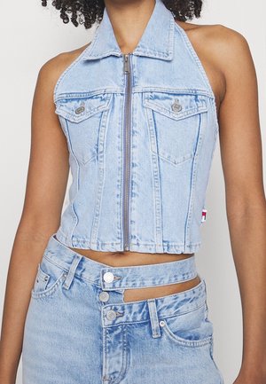 Kobieta nosząca jasnoniebieski jeansowy top na suwak typu halter, połączony z dwutonowymi niebieskimi jeansami z podwójnym paskiem w talii.