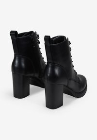 Botas de cuero negras hasta el tobillo con un tacón alto y grueso, parte delantera con cordones, cremallera lateral y suelas texturizadas para un mejor agarre.