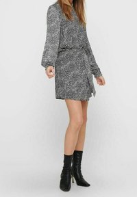 Vestido de estampado en blanco y negro con mangas largas, cintura ajustada y diseño cruzado, combinado con botines negros de tacón.