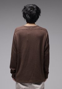 Chemise marron à manches longues en tricot gaufré avec un col rond, une coupe ample et des épaules tombantes. Tissu texturé avec détail de col côtelé visible.