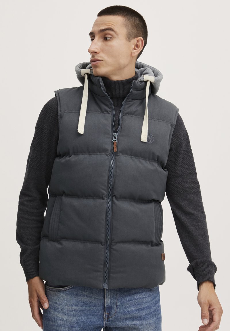 Puffer vest i mørkegrå med glidelås, justerbar grå hette og kontrastfarget off-white snor. Strukturert stoff med sidelommer.