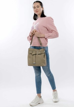 Tan handbag with a belt accent and silver hardware. Worn with a pink sweatshirt and distressed blue jeans, paired with white sneakers.