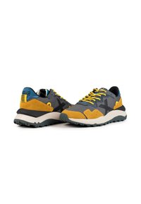 Zapatillas multicolores con parte superior de malla gris, acentos de ante amarillo, detalle de logo negro, suela media blanca gruesa y suela de goma texturizada.