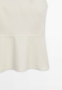 Tissu beige clair avec un détail de couture et un ourlet à basque, montrant la texture et la matière lisse sur un fond blanc.