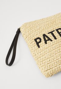 Gul vävd väska med svart broderad text "PAT." Har ett svart läderhandtag och en strukturerad, halmsliknande yta.