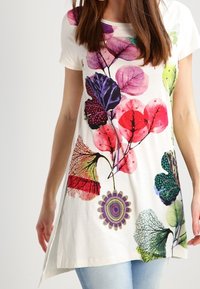 Vit tunika med en färgglad botanisk tryck med olika blad i rosa, grönt och lila. Kortsleeves och en lös passform.