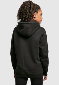 Sudadera con capucha negra de textura suave, bolsillo canguro y puños acampanados. Presenta un corte holgado y capucha ajustable con cordones.