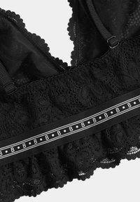 Soutien-gorge en dentelle noire avec motifs floraux, bords festonnés, bretelles ajustables et une bande décorative ornée de pois blancs et d'un motif en forme de lettre « B ». 