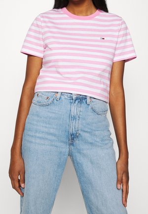 Mujer con una camisa de manga corta de rayas rosas y blancas metida en unos vaqueros de cintura alta de color azul claro.