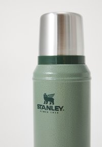 Vihreä eristetty ruostumattomasta teräksestä valmistettu termos, jossa on teksturoidut pinnat, hopeinen kansi ja musta logo, jossa lukee "STANLEY vuodesta 1913."