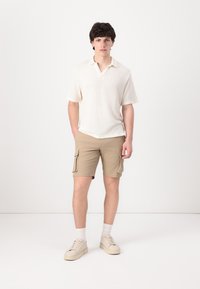 Lys beige kortermet polo skjorte med teksturert stoff, kombinert med khaki cargo-shorts med sidelommer. Nøytral-tonede sneakers fullfører looken.