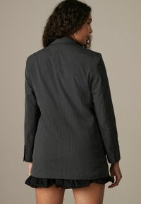 Šedý pruhovaný blazer s přiléhavým střihem, jednobarevný, s klopovým límcem a dlouhými rukávy. Obsahuje knoflíkové manžety a hladkou texturu.