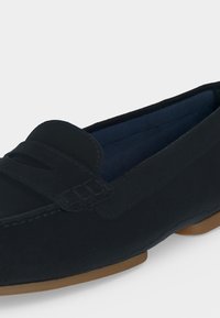 Μοκασίνι από σκούρο μπλε δέρμα με λεπτομέρεια λουριού penny και ανοιχτό καφέ λαστιχένια σόλα, πλαγία πλευρική όψη σε λευκό φόντο.