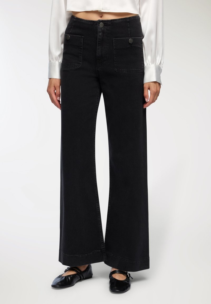 Szerokie czarne dżinsowe spodnie z przednimi kieszeniami, zapięciem na guzik i kontrastującymi detalami w stębnowaniu. Teksturowana tkanina o czystym wykończeniu.