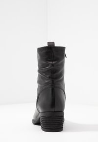 Bottine en cuir noir avec un tige légèrement froncée, bout rond et talon bloc texturé. Dotée d'une languette à l'arrière et d'une fermeture éclair sur le côté.