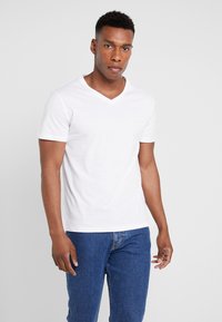 Hvid kortærmet V-hals t-shirt lavet af bomuld, med en glat tekstur og en afslappet pasform, parret med blå denim jeans.