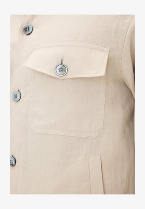 Beige linnen shirt met twee borstzakken, elk met een enkele knop. Gelaagd stof met een natuurlijke weving en zichtbare stiksels.