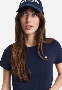 Navy blue cotton t-shirt with short sleeves, featuring a small logo on the chest. Worn with a matching navy cap displaying white text.